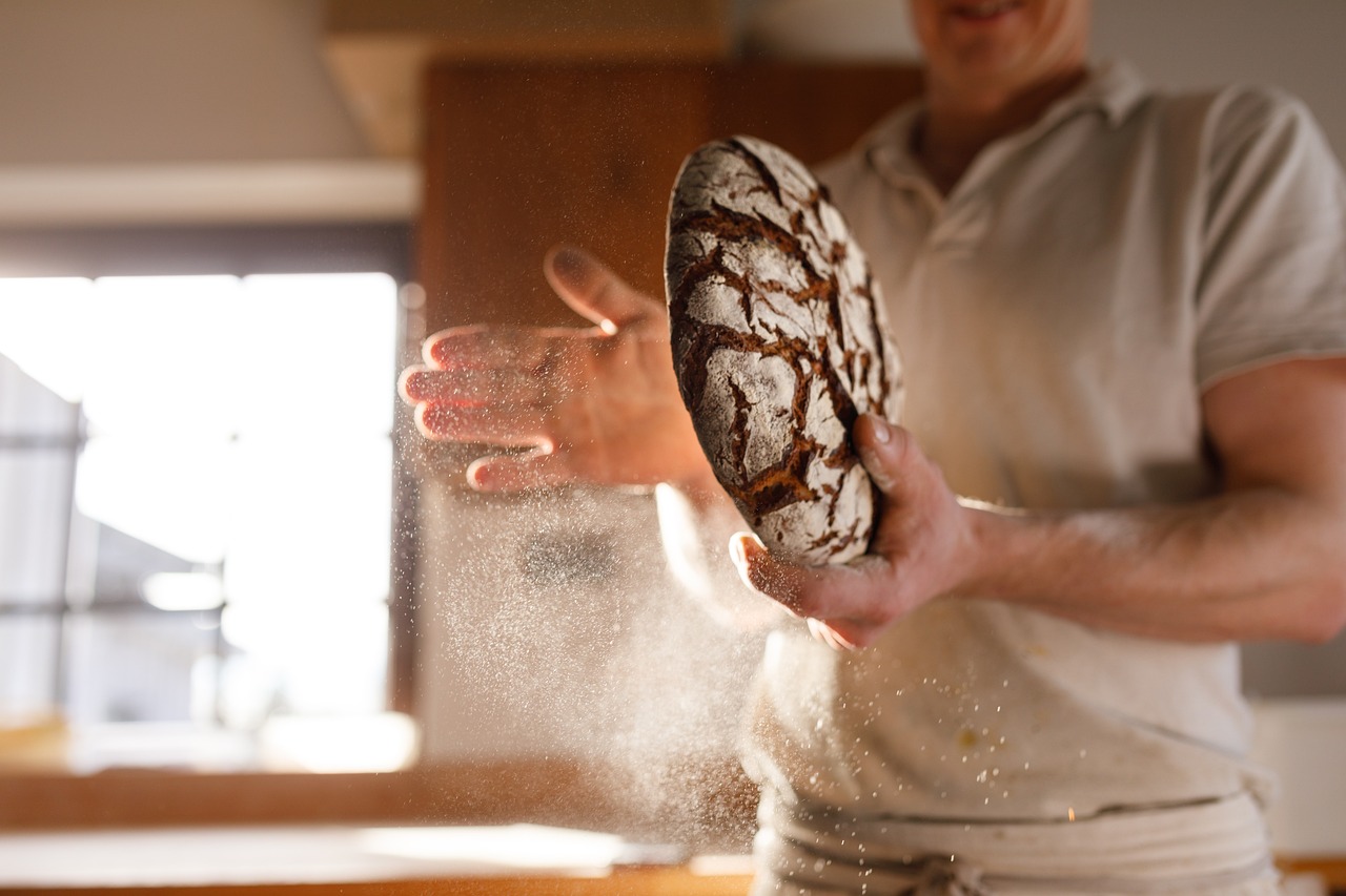 baker A baker standing in a room tapping some excess flour off of a bread load of some kind.